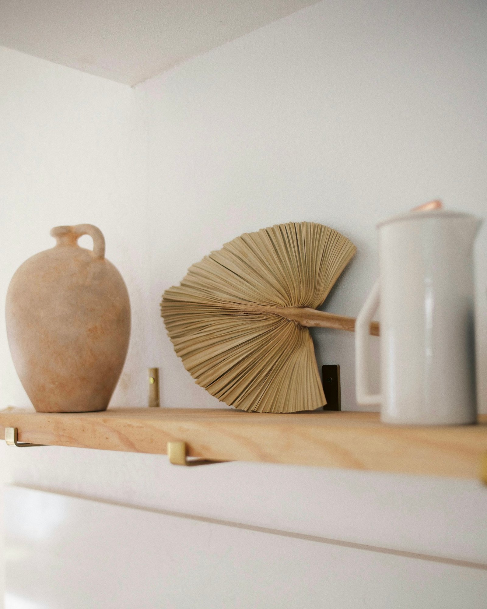 Objets en céramique et éventail en paille posés sur une étagère en bois