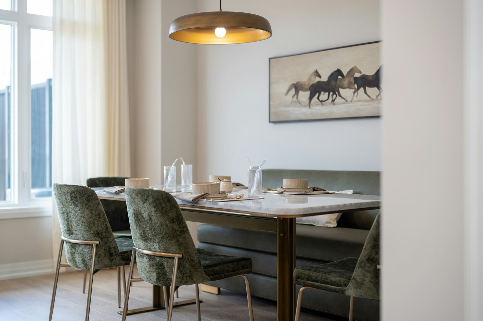 Salle à manger lumineuse, banquette verte et tableau de chevaux