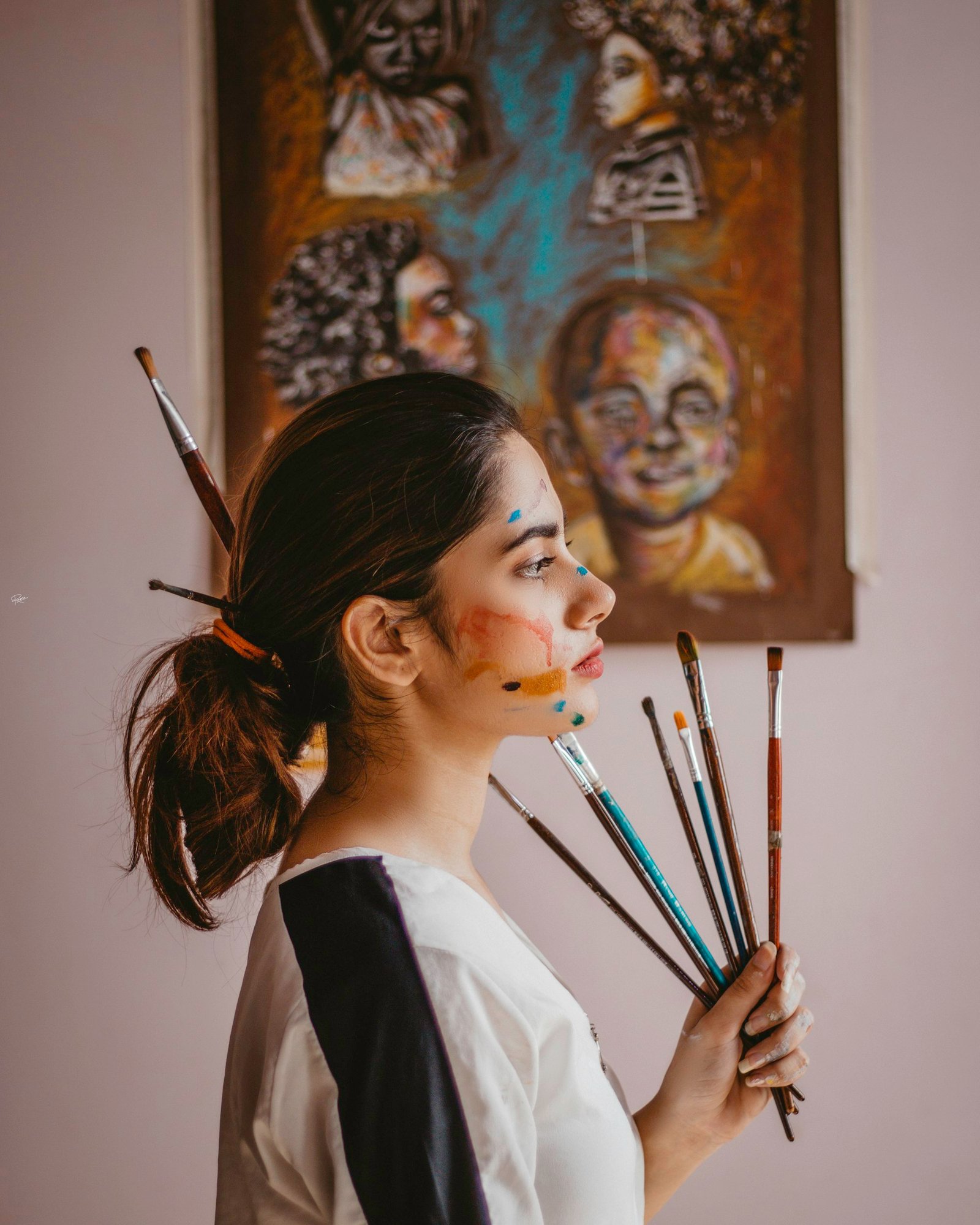 Artiste tenant une poignée de pinceaux devant ses toiles